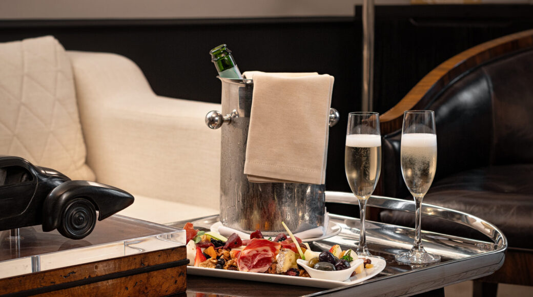 NZ6_8750-Edit Luxury hotel lounge table with chilled champagne, two flutes, charcuterie, olives, and a cream sofa.