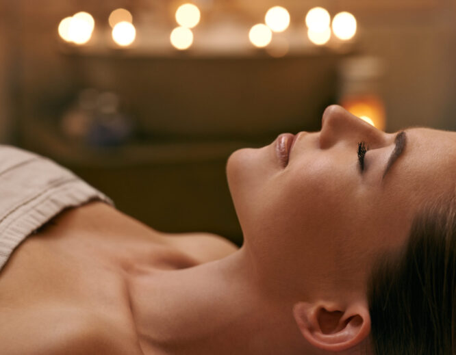 Savoring the moment Woman relaxing with eyes closed during a spa facial in a softly lit treatment room.