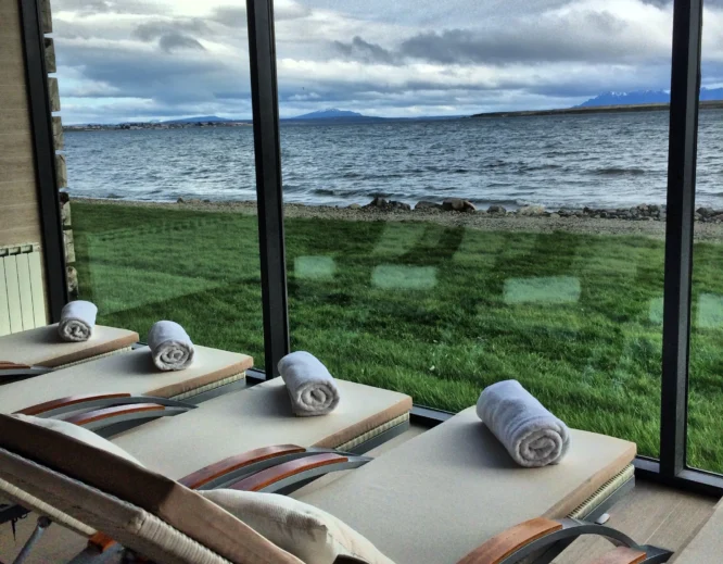 singular-spa-wordpress Lounge chairs with rolled towels overlook a windswept lake and distant mountains through floor-to-ceiling windows.